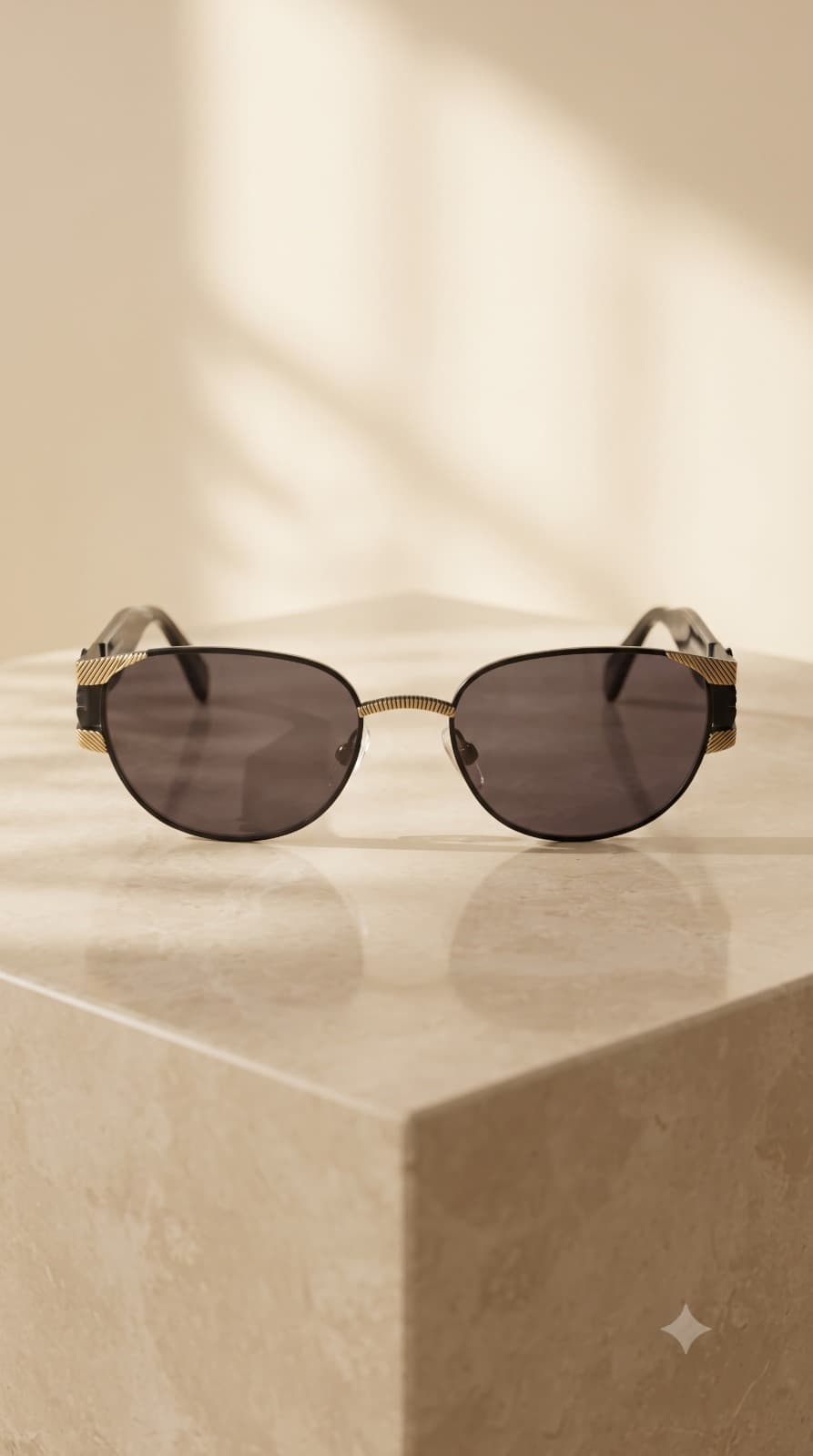Vintage black and champagne-gold eyewear on a warm stone pedestal